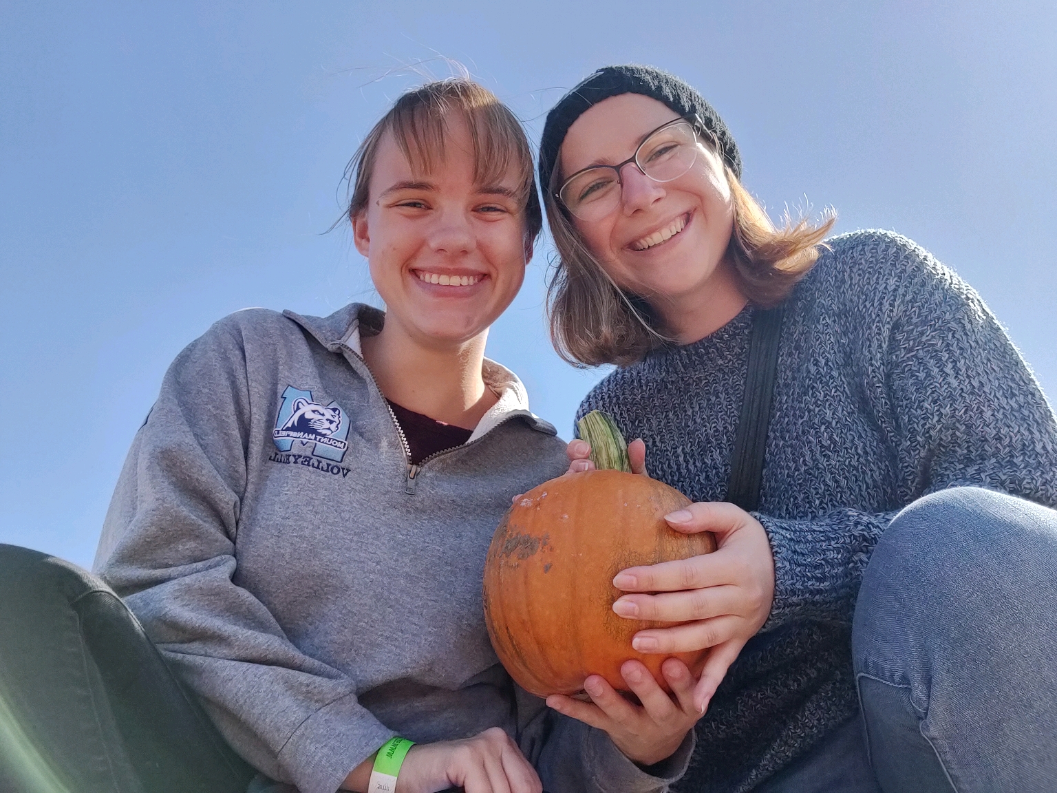 Two women in the DRC Peer Mentor Program pose with a Pumpkin while looking down at the camera. 
